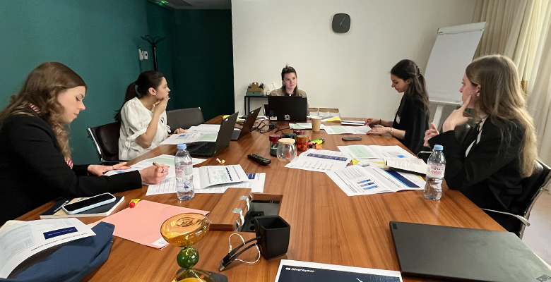 Group of women seated around a table working on laptops and documents, engaged in discussion during a consulting event or workshop session.
