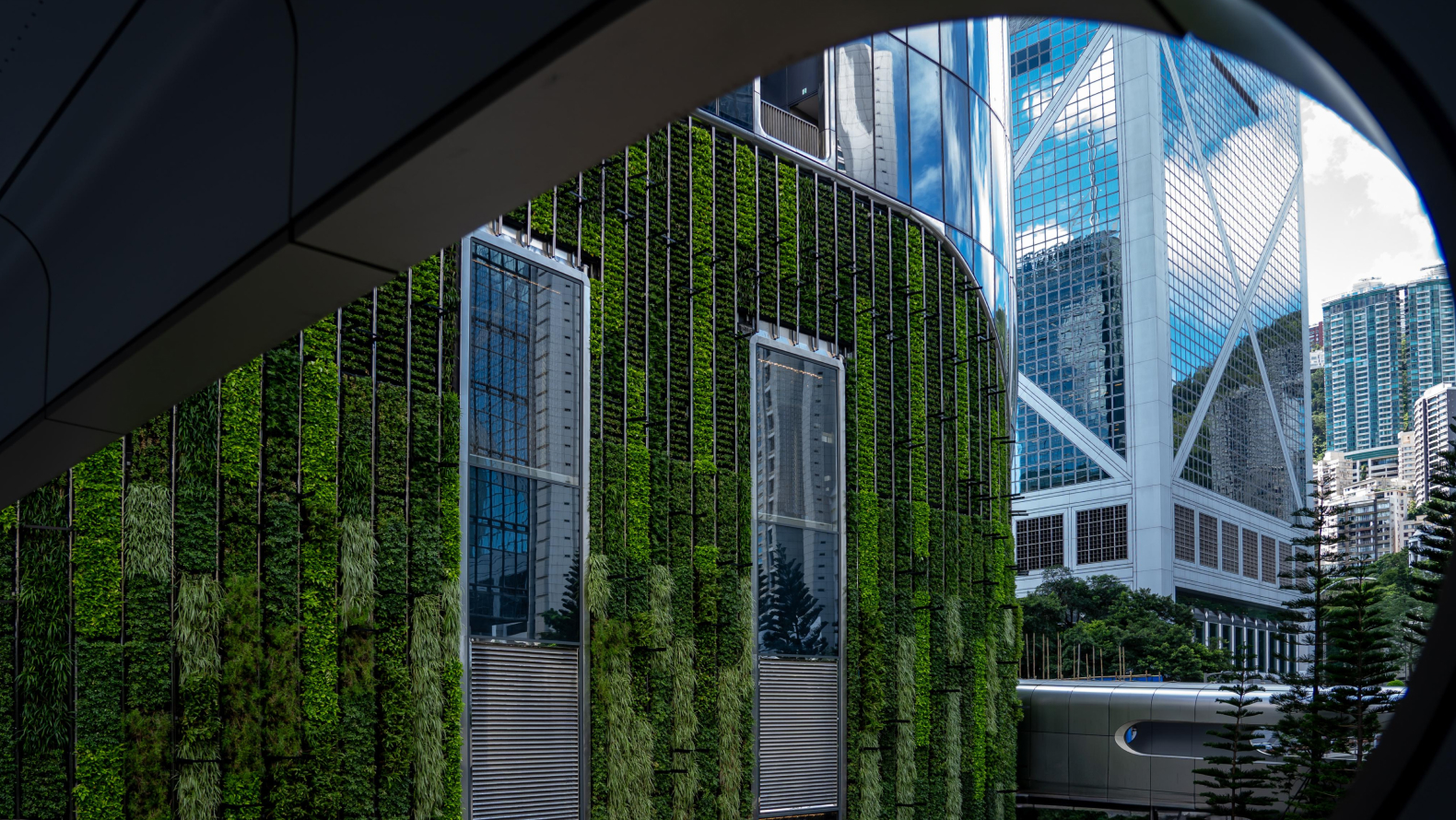A modern building with a vertical green wall surrounded by glass skyscrapers.