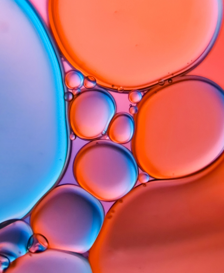 Close-up of colorful oil droplets in water, showing overlapping translucent bubbles in shades of blue, purple, and orange.