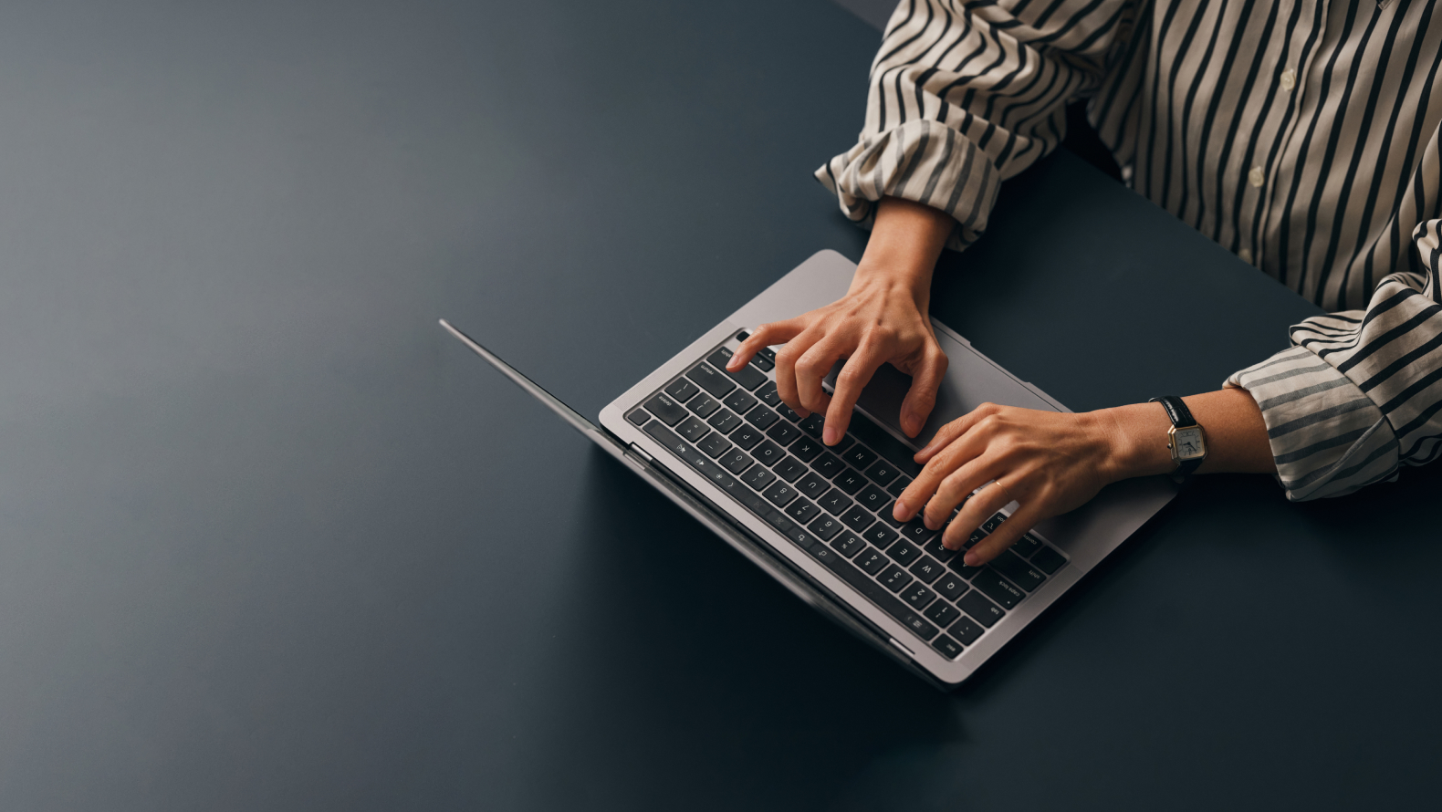 Photography of an open laptop and the arms of a person writing with the keyboard.