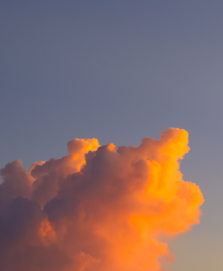 A large cloud illuminated with warm orange light against a clear sky.