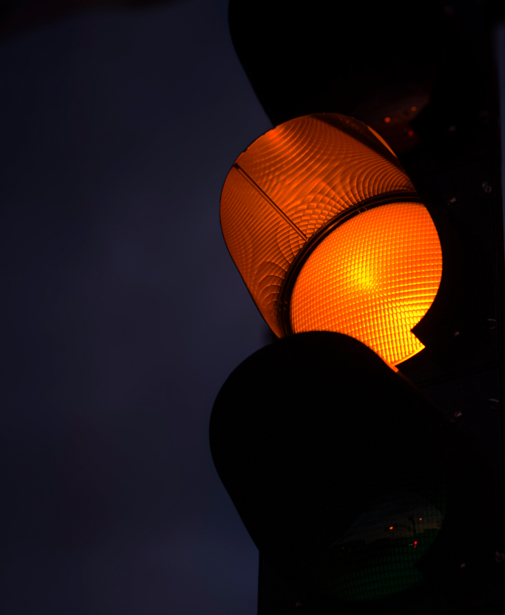 Close-up of an illuminated amber traffic light glowing against a dark night sky.