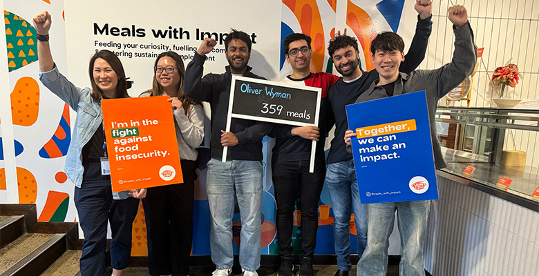 Volunteers from Oliver Wyman APR team holding signs and raising fists supporting fight against food insecurity.