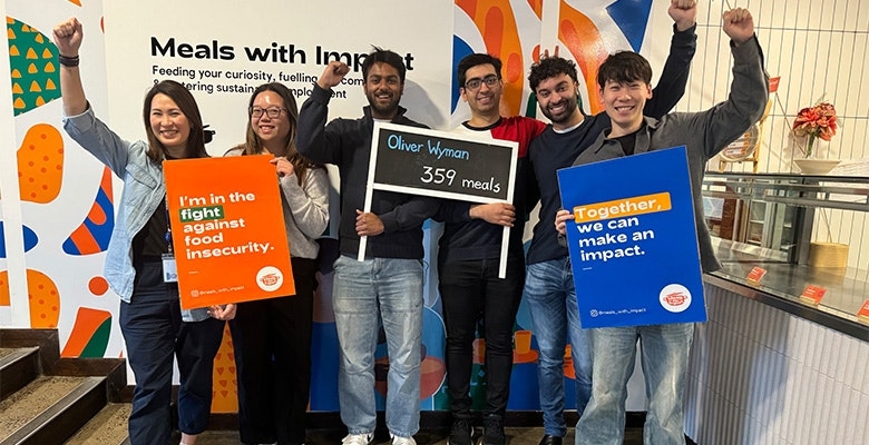 Volunteers from Oliver Wyman APR team holding signs and raising fists supporting fight against food insecurity.