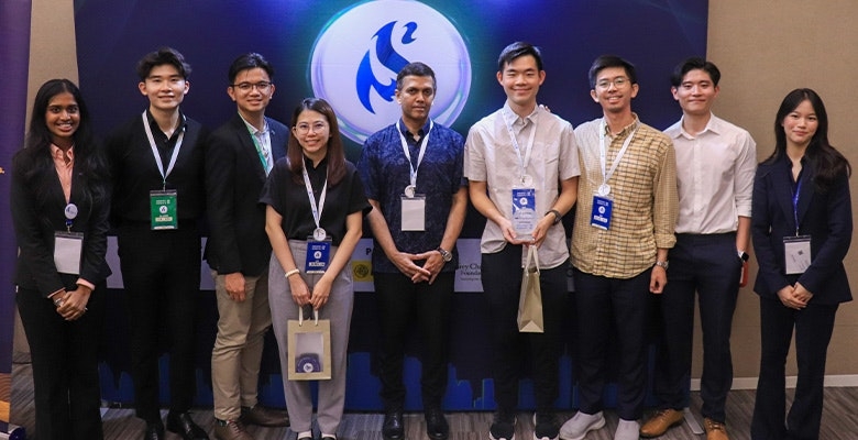 Nine people in formal attire stand with certificates and gift bags at an award event, posing in front of a branded backdrop with conference badges.