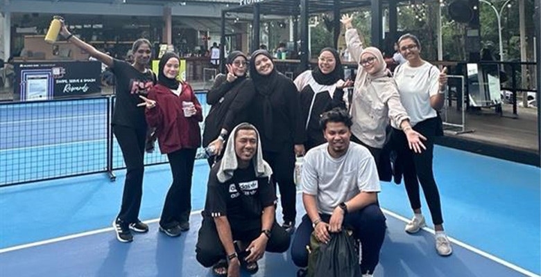 Colleagues posing on a blue outdoor tennis court during the Kuala Lumpur virtual firm day.