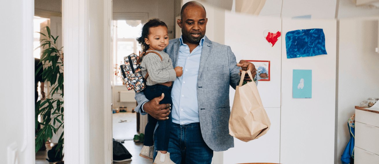 Father carries a baby and a grocery bag upon his return home from shopping