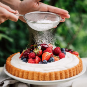 Person sprinkling sugar on top of fruit dessert