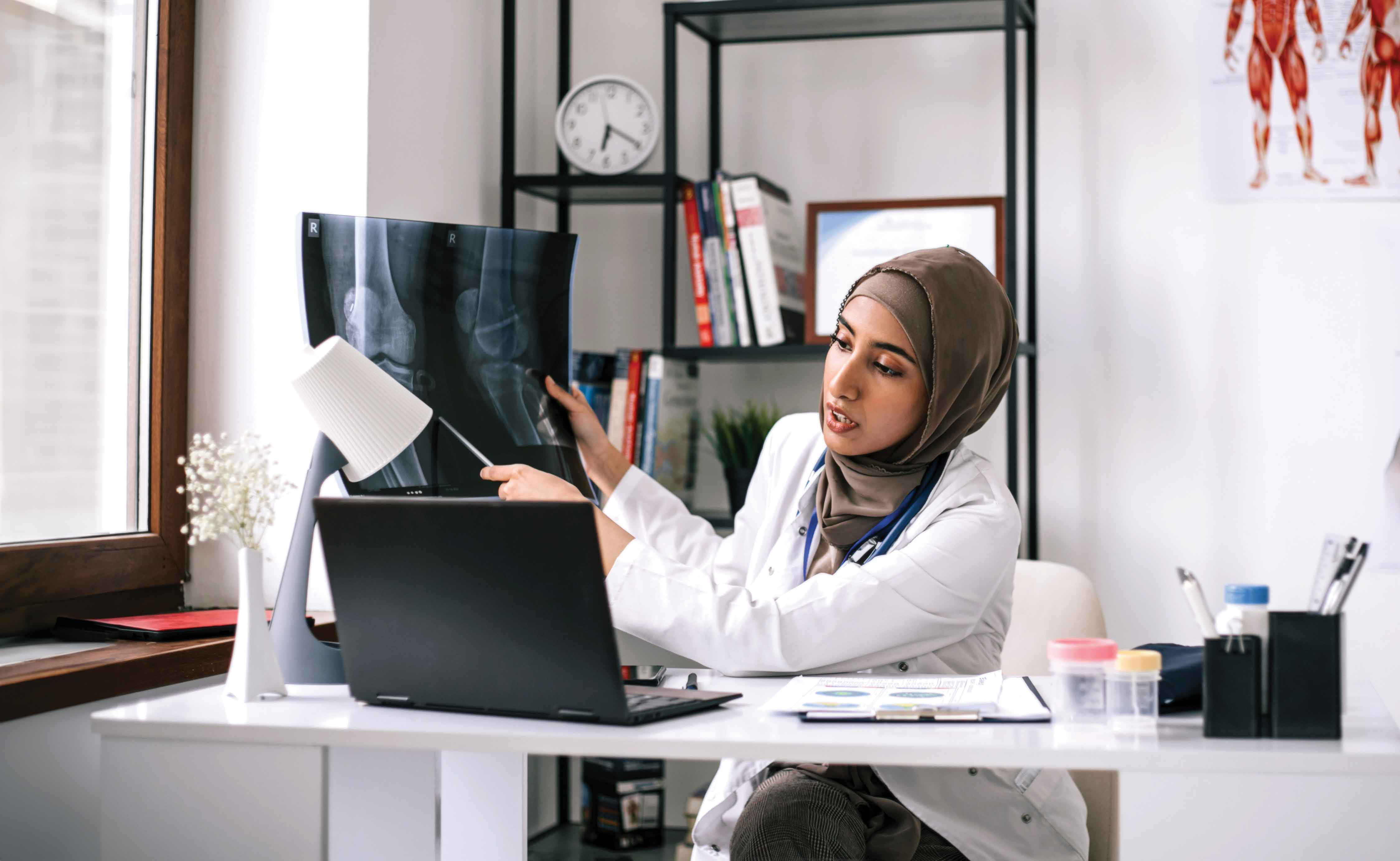 Picture of a female doctor holding up an X-ray and talking to someone on a computer