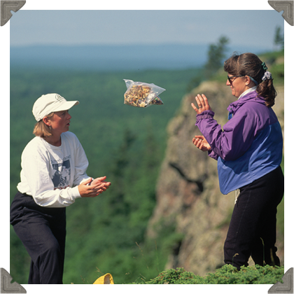a picture of two woman throwing and catching a bag on a hill